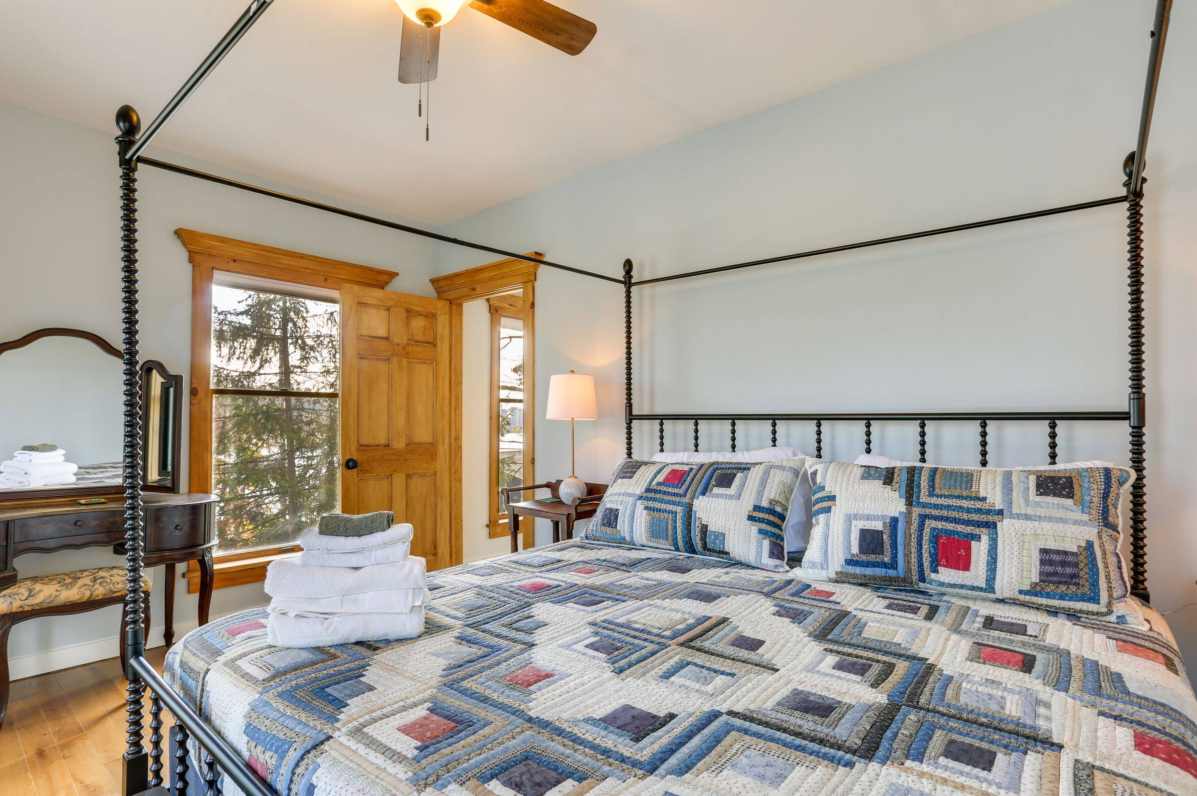 The primary bedroom: a four-poster king bed under a patchwork quilt beside a bright window.