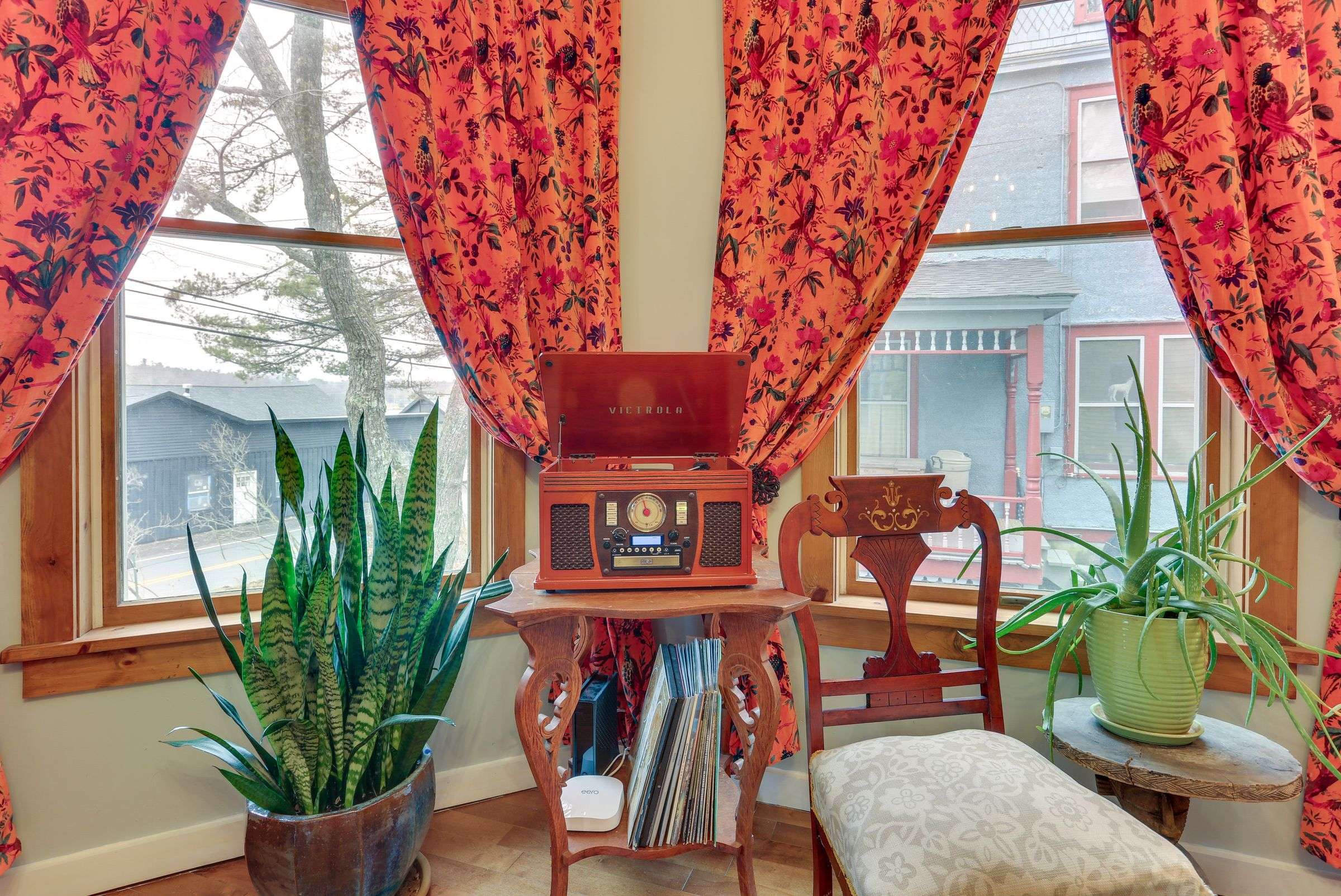 A record player and stack of vinyl on an antique table in the bay window, framed by floral curtains.