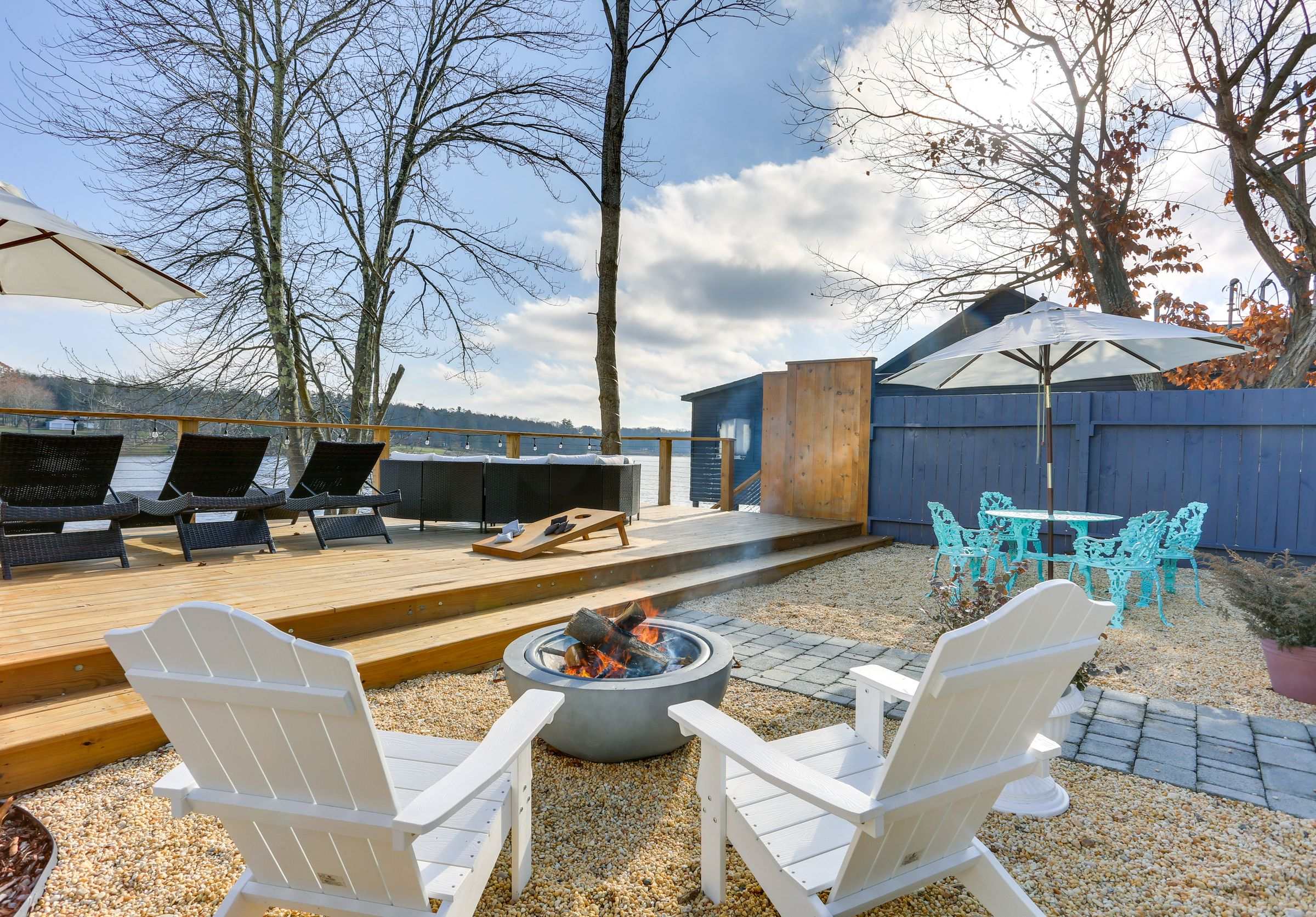 Adirondack chairs around a fire pit on the pebbled patio, with the lake deck, hot tub and café seating beyond.