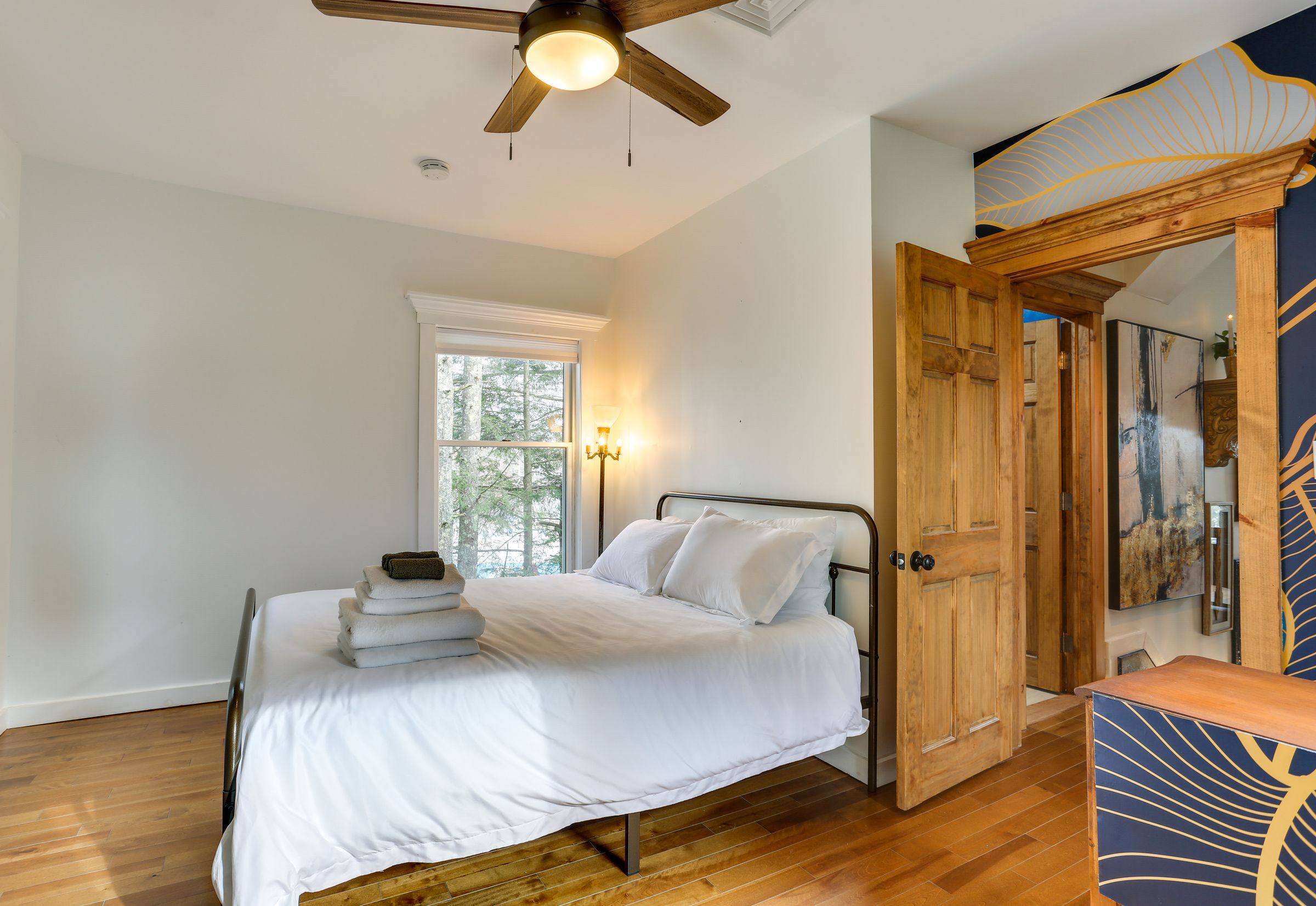 The second bedroom with a queen bed, iron frame and fresh linens beside a woodland window.
