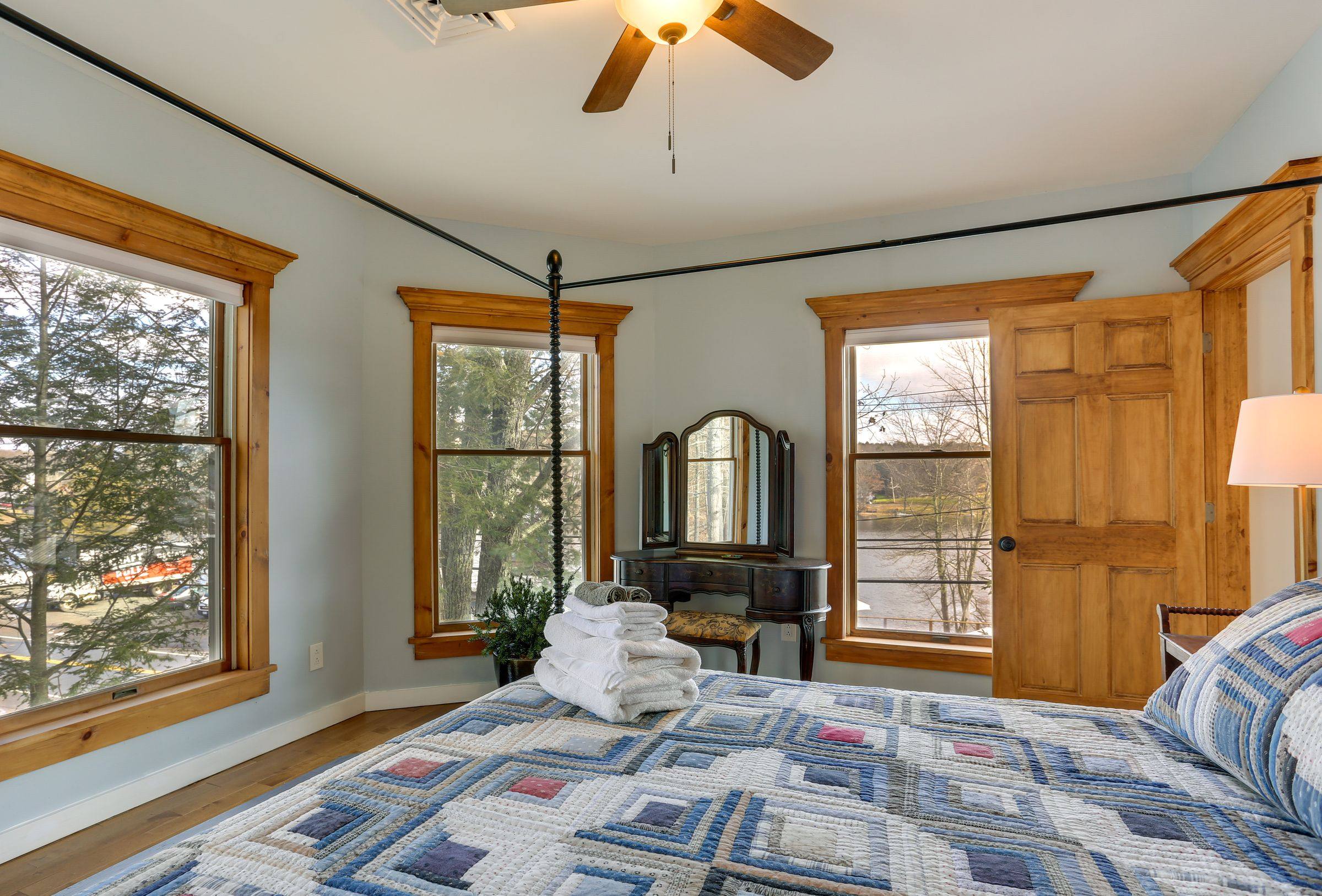 The primary bedroom's corner windows looking out toward the lake and the trees.